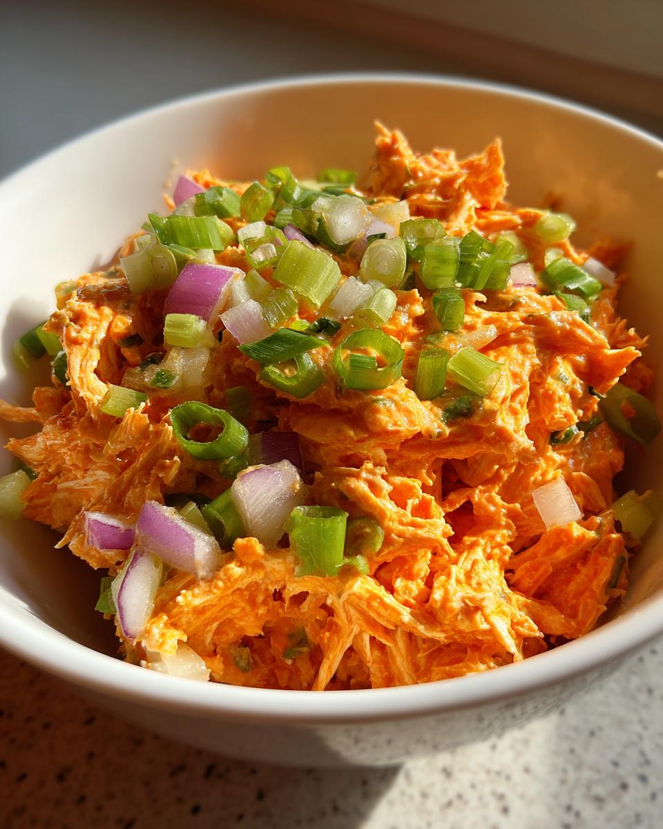 A bowl of 10 Minute Buffalo Chicken Salad Quick Flavorful Delight topped with chopped green onions and red onion.