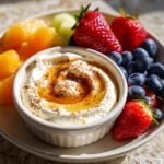 A bowl of 5 Minute Healthy Yogurt Fruit Dip topped with honey and cinnamon, served with fresh strawberries, blueberries, and melon.