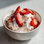 Een kom met romige aardbeienroom, gegarneerd met verse aardbeienstukjes. Perfect voor het Strawberry Cream Recept.