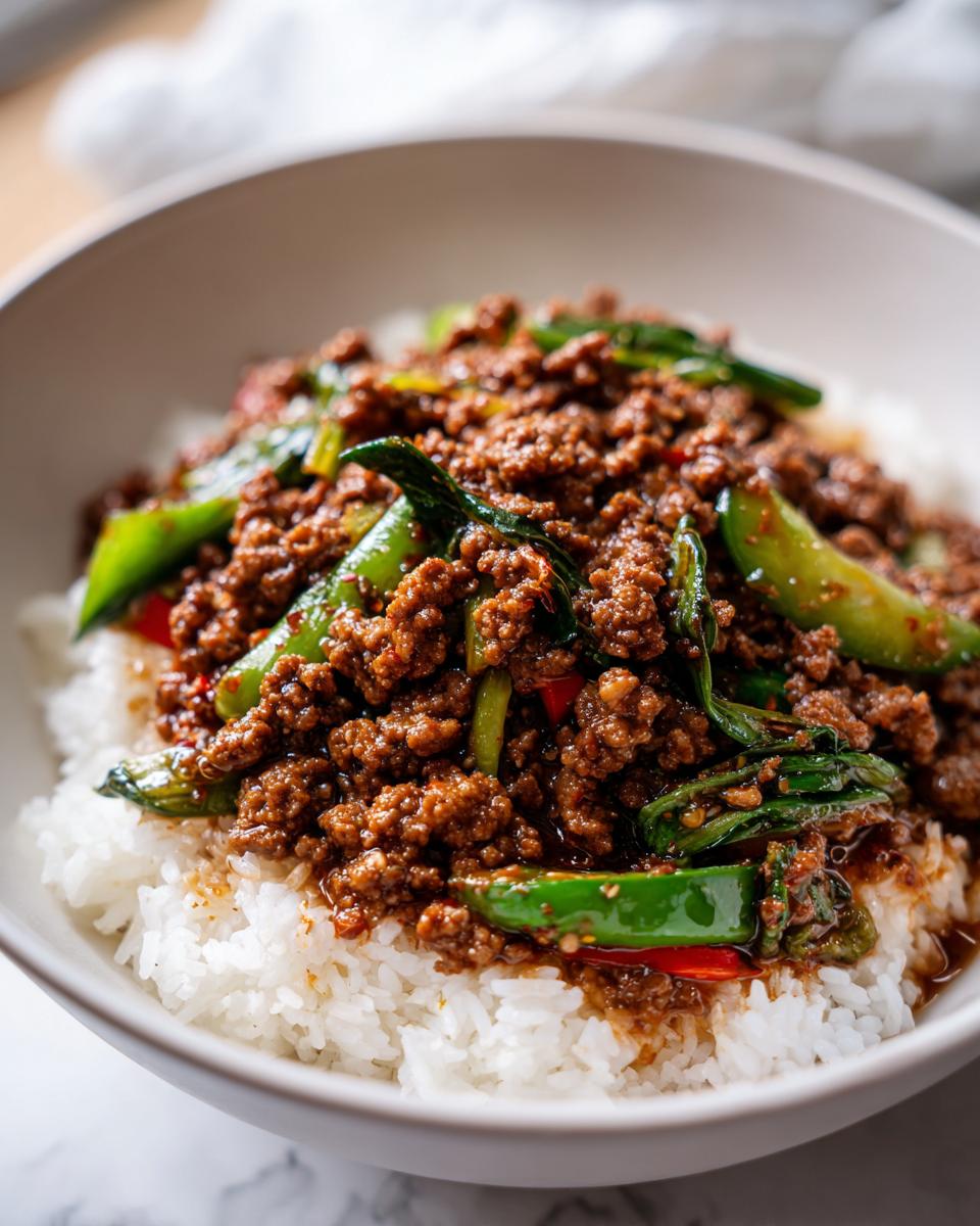 Close-up of a bowl of fluffy white rice topped with savory Asian ground beef and green peppers.