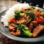 A close-up of a plate of beef stir fry with broccoli, red peppers, and white rice. This is one of our 10 Irresistible Beef Stir Fry Recipes.