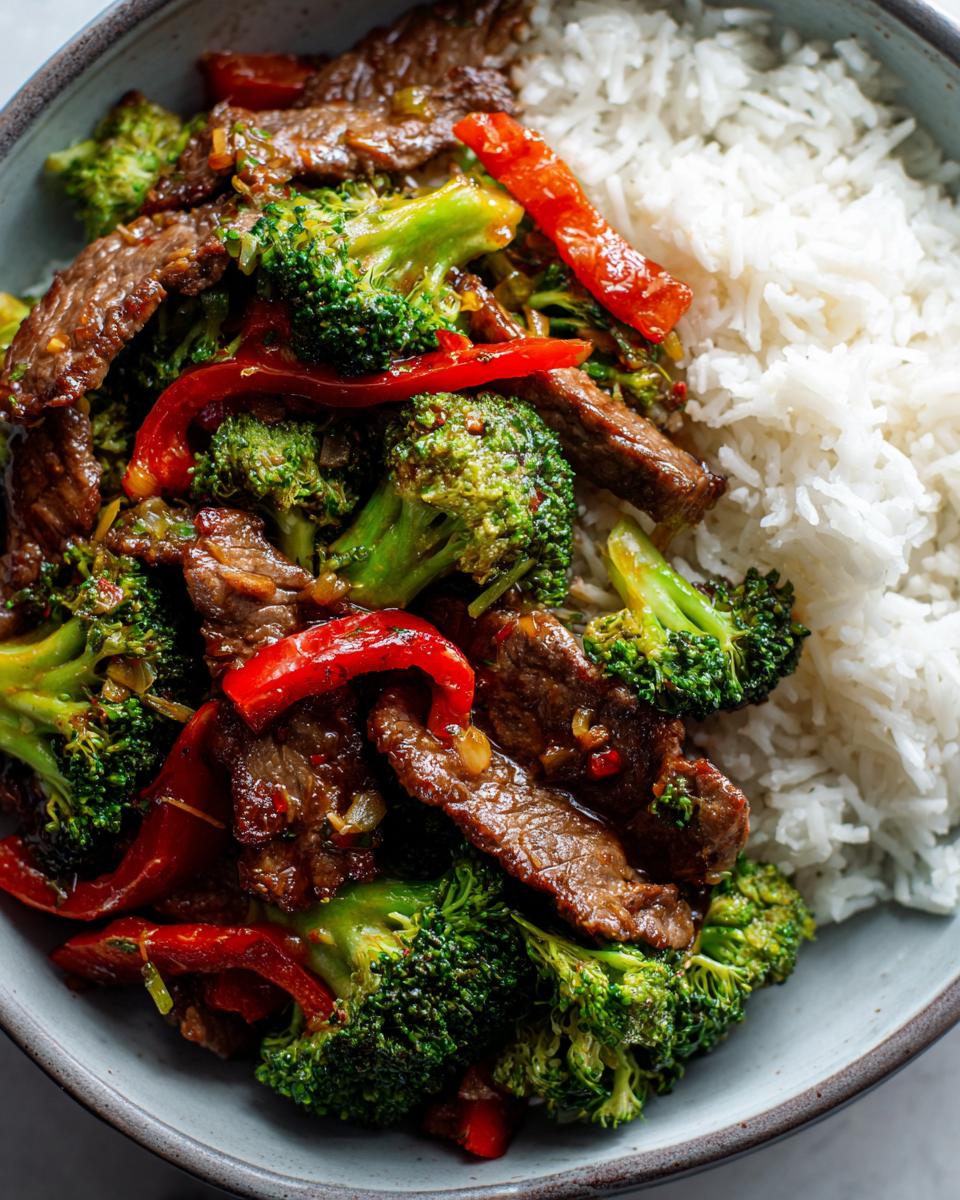 Close-up of a bowl of beef stir fry with broccoli, red peppers, and fluffy white rice.