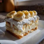 A slice of creamy banana pudding with layers of vanilla wafers, pudding, and whipped cream, topped with fresh banana slices.
