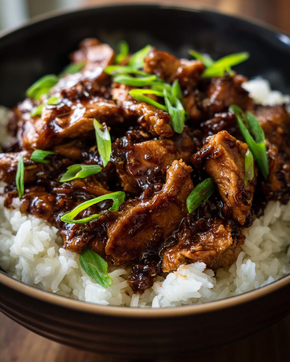 Close-up van de Beste Slow Cooker Bourbon Kip geserveerd op witte rijst, gegarneerd met lente-ui.