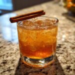 Een close-up van een Candy Apple Shot met ijs en twee kaneelstokjes als garnering.