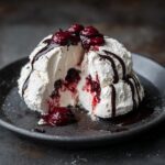 A decadent cream cheese dessert, cut open to reveal a berry filling, drizzled with chocolate sauce and topped with berries.
