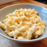 A close-up of a bowl filled with creamy cottage cheese mac and cheese, topped with melted cheddar.