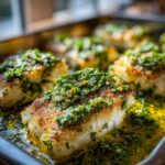 Close-up of a piece of crispy baked fish topped with a vibrant lemon herb sauce.