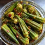 Close-up of a jar filled with crunchy pickled okra, chili flakes, dill, and mustard seeds.