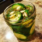 Close-up of a glass jar filled with crunchy refrigerator pickles, dill, garlic, and pickling spices.