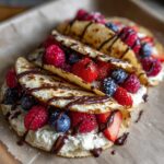 Close-up of delicious cheesecake tacos filled with fresh berries and drizzled with chocolate sauce.