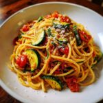 A close-up of a bowl of Delicious Tomato Zucchini Pasta, featuring spaghetti, sliced zucchini, and cherry tomatoes, topped with grated cheese.