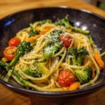 A close-up of Delightful Pasta Primavera, featuring spaghetti tossed with broccoli, cherry tomatoes, carrots, and asparagus, topped with grated Parmesan.