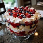 A beautiful Festive 4th Of July Trifle layered with cake, cream, strawberries, and blueberries, topped with whipped cream and more berries.
