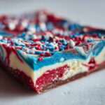 A close-up of a slice of Festive Red White Blue Bark, swirled with red, white, and blue chocolate and topped with sprinkles.