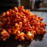 A close-up shot of a pile of spicy Firecracker Popcorn, coated in a vibrant red seasoning.