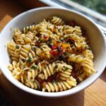 Close-up of a bowl filled with flavorful cold pasta salad with Italian dressing, featuring fusilli pasta, sun-dried tomatoes, and herbs.