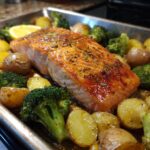 A close-up of a flavorful sheetpan salmon and potatoes with veggies, featuring a perfectly cooked salmon fillet surrounded by roasted potatoes and broccoli.