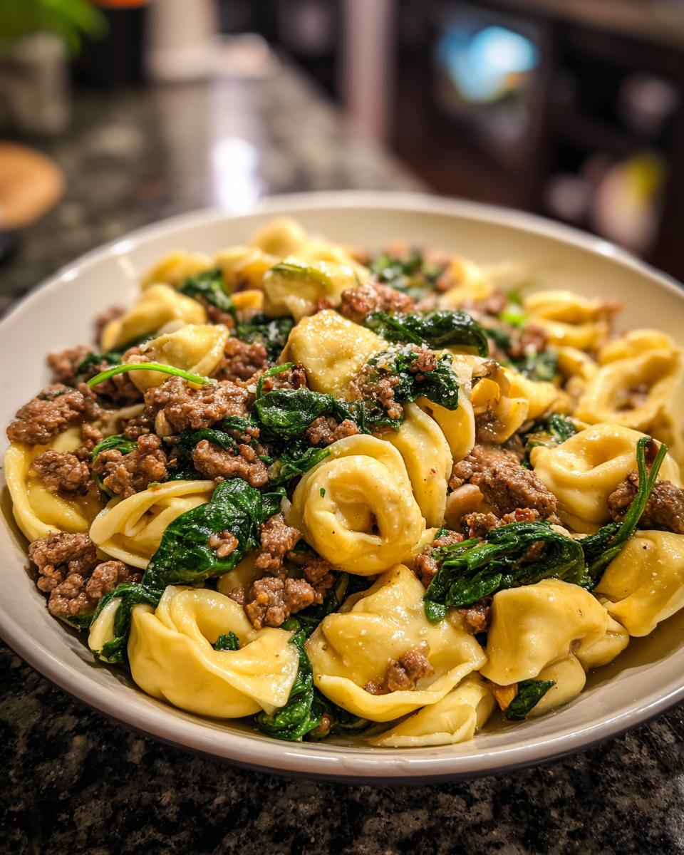 A close-up of a bowl filled with Irresistible Garlic Butter Beef and Spinach Tortellini, showing plump tortellini pasta mixed with seasoned ground beef and wilted spinach.