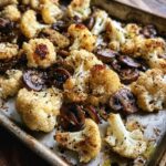 Close-up van gebakken bloemkool met champignons op een bakplaat, gekruid met zwarte peper.