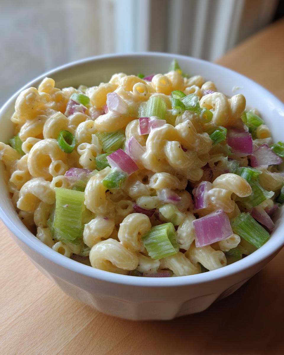 Close-up of Guy Fieris Macaroni Salad, featuring elbow pasta, celery, red onion, and green onions in a creamy dressing.