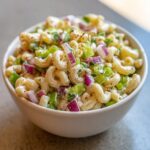 A close-up of Guy Fieris Macaroni Salad Recipe, featuring elbow pasta, red onion, celery, and a creamy dressing.