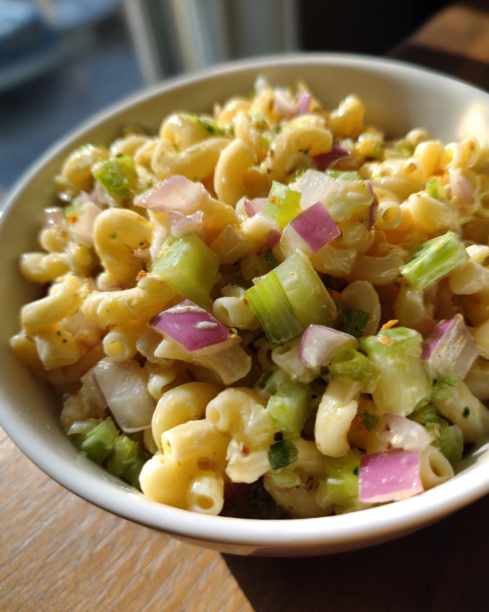 Close-up of Guy Fieris Macaroni Salad Recipe in a white bowl, featuring elbow macaroni, diced celery, and red onion.