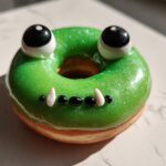 Een Halloween Monster Donut in de vorm van een groene kikker met glimmende glazuur en grote ogen.