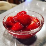 Een glazen kom gevuld met heerlijke, glanzende homemade aardbeiensaus en verse aardbeien.
