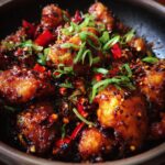 Close-up of Irresistible Black Pepper Chicken, coated in a glossy sauce with chili flakes and green onions.