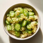 A bowl of Irresistible Dill Pickle Pasta Salad featuring rotini pasta, sliced cucumbers, and fresh dill.