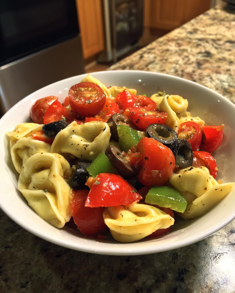 A bowl of Irresistible Easy Italian Tortellini Pasta Salad with cherry tomatoes, olives, and green peppers.