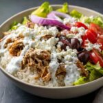 Close-up of an Irresistible Greek Chicken Gyro Bowl featuring shredded chicken, rice, feta cheese, tomatoes, olives, and tzatziki sauce.