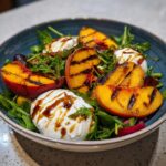 Close-up of an Irresistible Grilled Peach Burrata Salad featuring grilled peach slices, creamy burrata cheese, and arugula, drizzled with balsamic glaze.