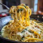 A fork lifting a generous portion of Irresistible Lemon Ricotta Pasta from a creamy sauce, garnished with herbs and cheese.