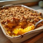 Close-up of a freshly baked mango crumble in a baking dish, with a fork digging into the juicy fruit and golden topping.