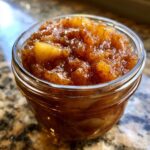Close-up of a small glass jar filled with Irresistible Pear Preserves, showing chunks of pear and spices.