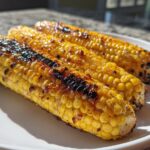 Drie gegrilde kolven maïs met Jalapeño Honing Boter, met geroosterde plekjes, op een wit bord.