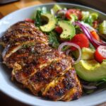 Gekruide kipfilet gesneden, geserveerd met een frisse salade van avocado, tomaat en rode ui.