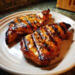 Two pieces of glistening, grilled mango chicken with char marks, served on a plate.