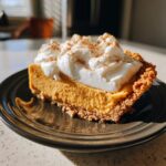 Een plak No-Bake Pumpkin Pie Delight met slagroom en kaneel op een donker bord.
