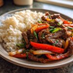 Bord met pittig roergebakken rundvlees, paprika, ui en lente-ui, geserveerd met witte rijst.