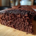 Een zacht stuk Poolse chocoladetaart met een rijke, donkere kleur, op een houten plank.
