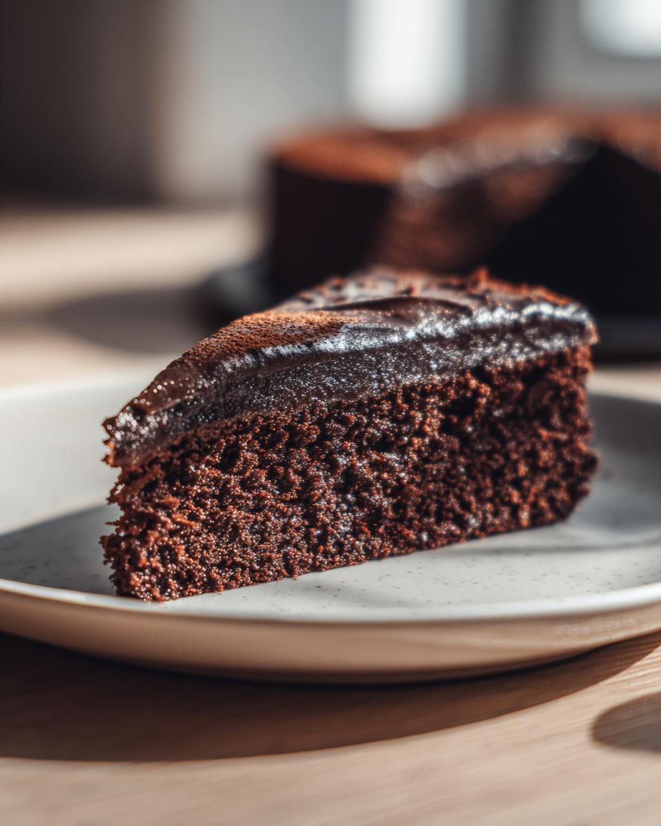 Een close-up van een stuk Poolse chocoladetaart met glanzende chocoladeglazuur en cacaopoeder.