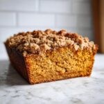 Een close-up van een Pumpkin Coffee Cake met een goudbruine streusel topping op een marmeren ondergrond.