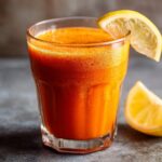 A glass of vibrant, freshly made carrot juice with a lemon wedge garnish, perfect for a healthy boost.