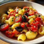 Close-up of a bowl filled with a refreshing Italian pasta salad, featuring pasta shells, halved cherry tomatoes, and black olives, garnished with parsley.