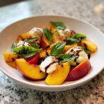Close-up of a refreshing peach burrata salad with fresh basil and a balsamic drizzle.