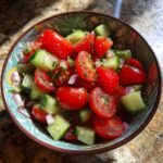 A colorful bowl of refreshing tomato cucumber salad with chopped red onion and herbs, perfect for summer.