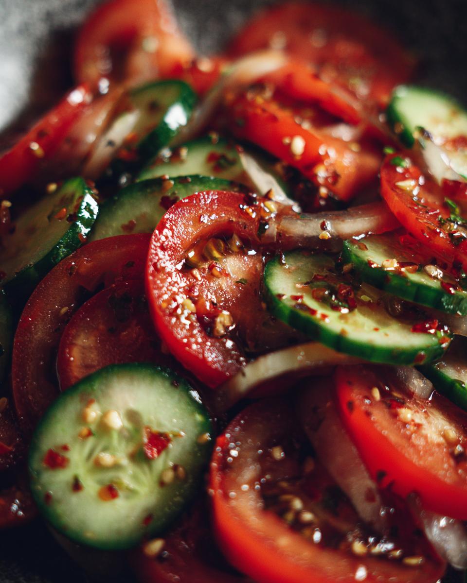 Close-up of a refreshing tomato cucumber salad with sliced red tomatoes, green cucumbers, and onions, seasoned with spices.